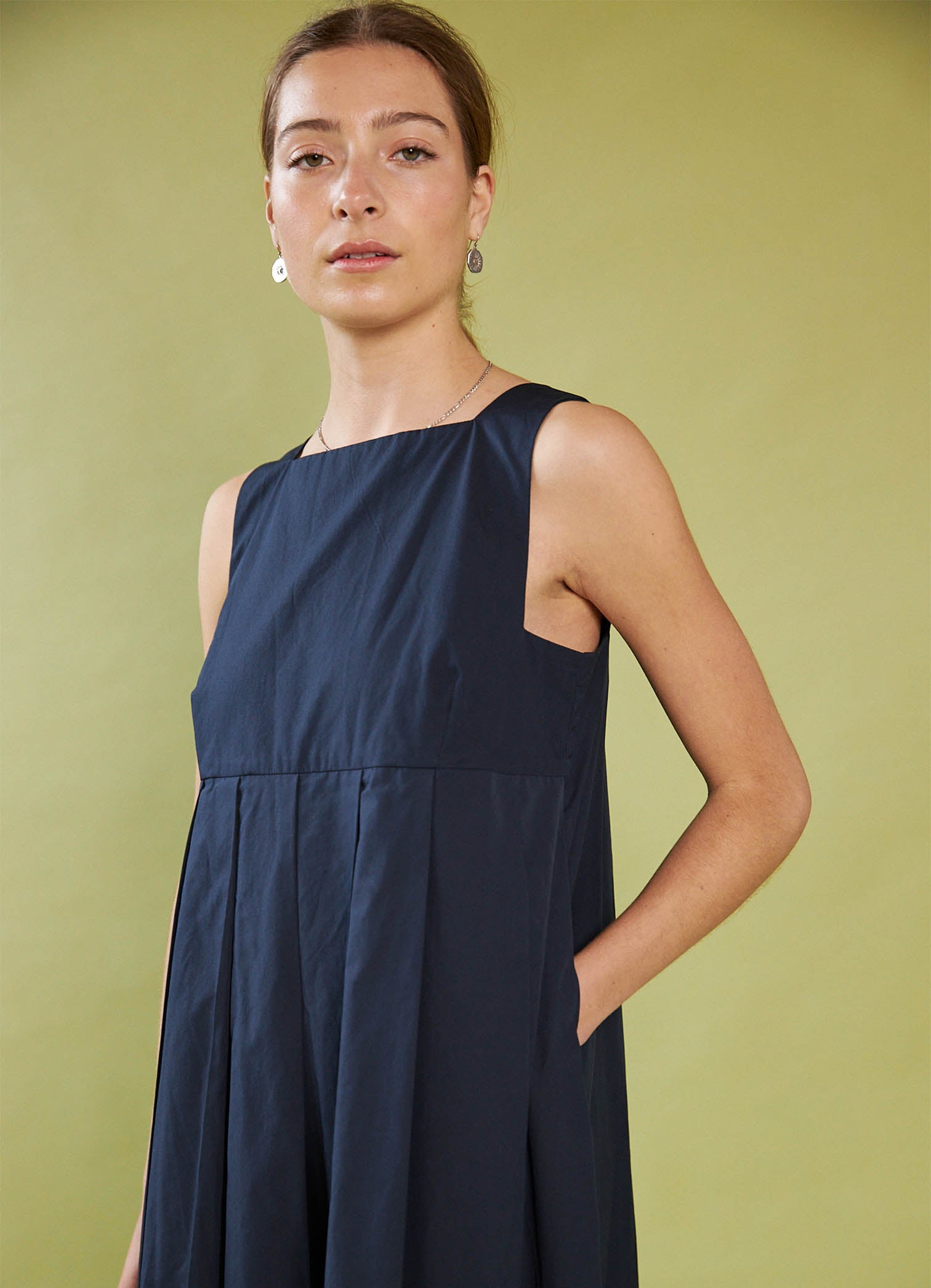 Woman wearing a Daylight Moon navy sleeveless dress against a green background
