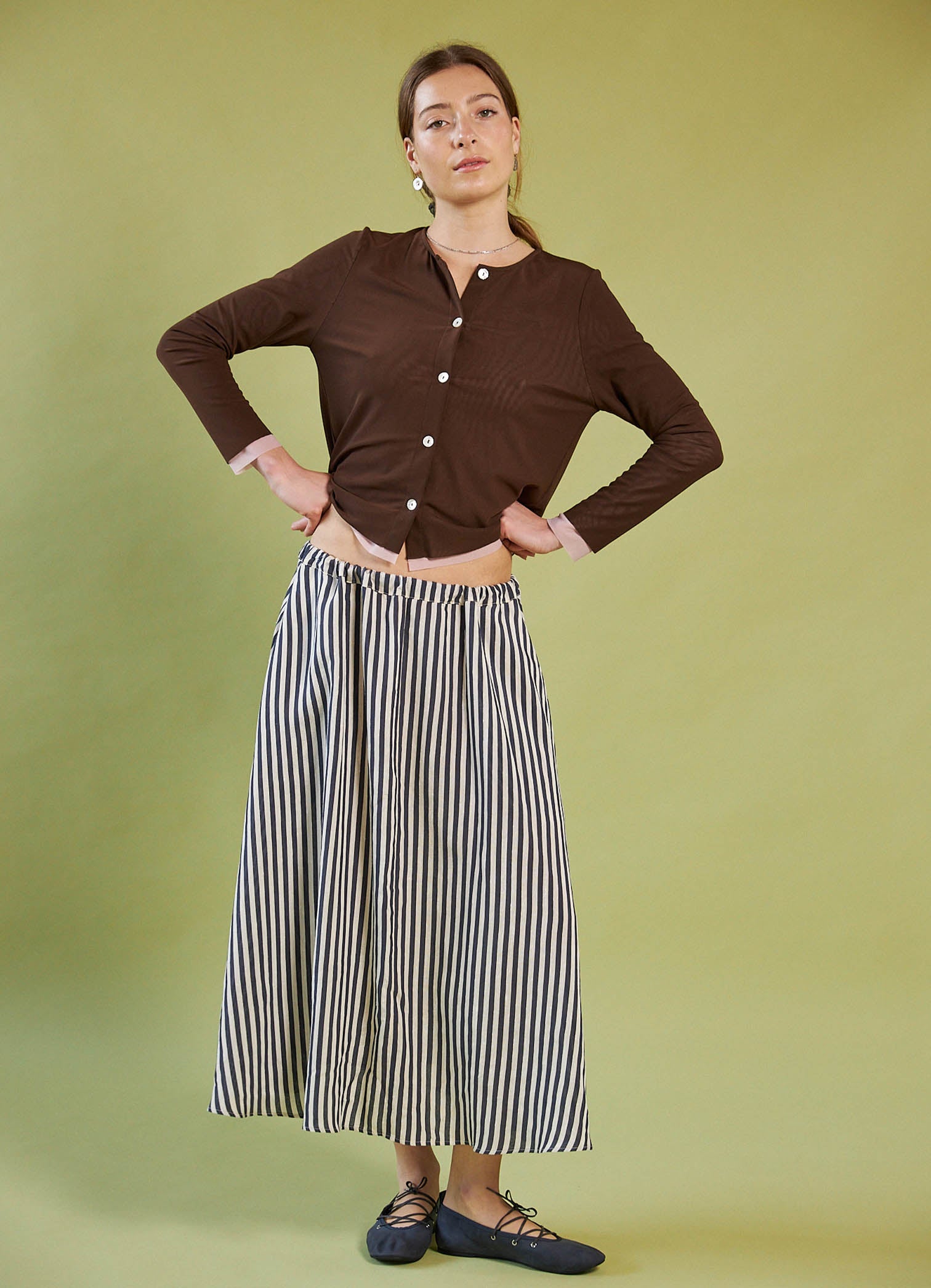 Woman wearing a Daylight Moon brown cropped cardigan and striped skirt on a green background
