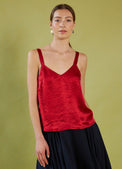 Woman wearing a Daylight Moon red camisole top and black skirt against a green background