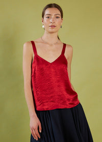 Woman wearing a Daylight Moon red camisole top and black skirt against a green background