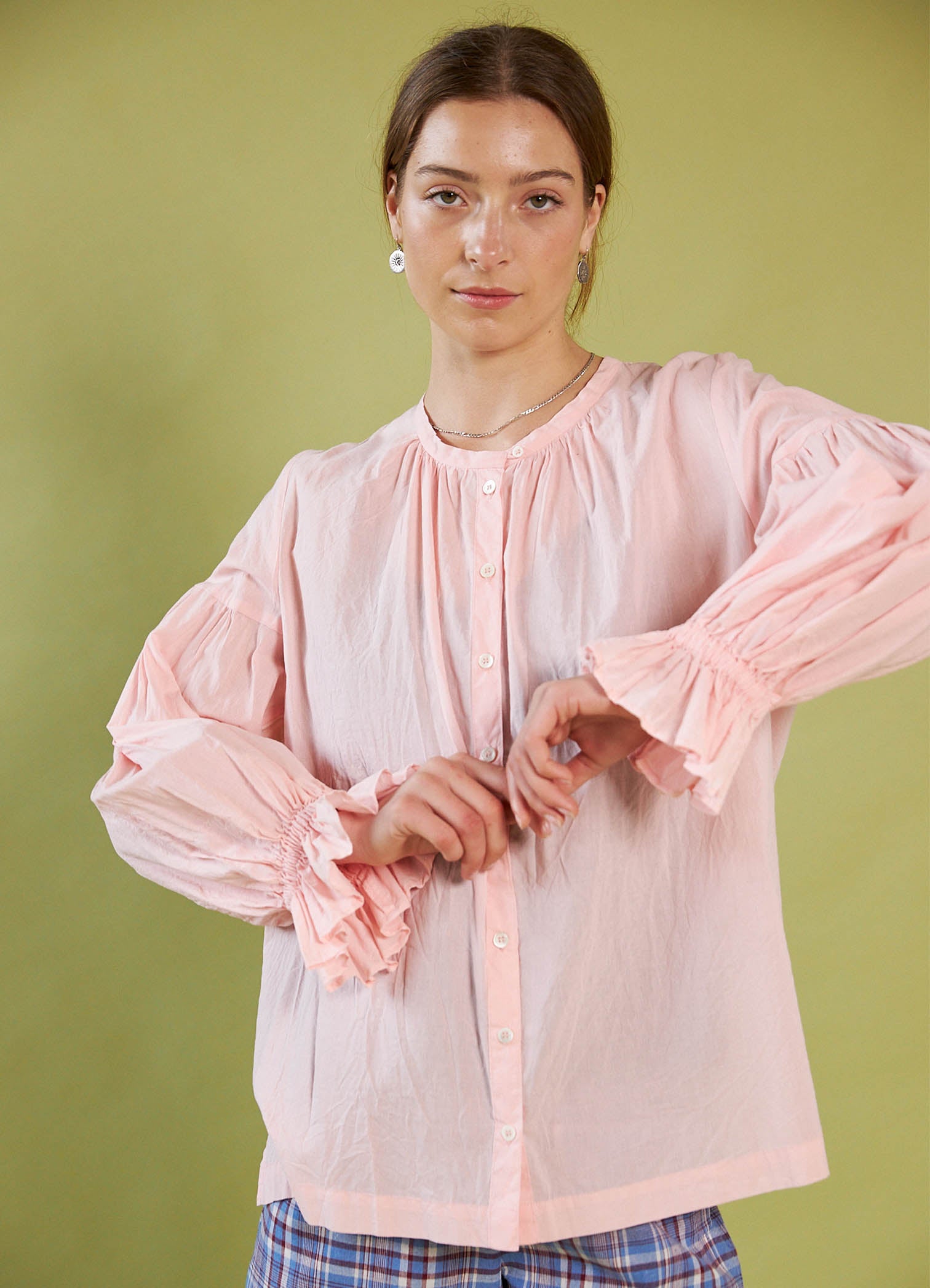 Woman wearing a Daylight Moon light pink blouse with puffed sleeves against a green background