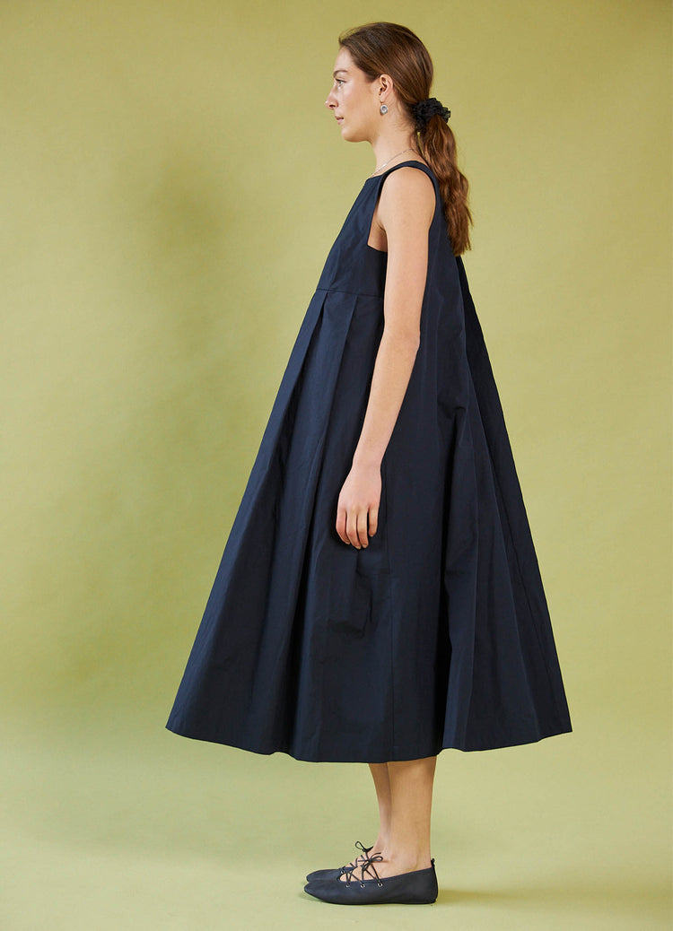 Woman wearing a Daylight Moon navy blue dress against a green background