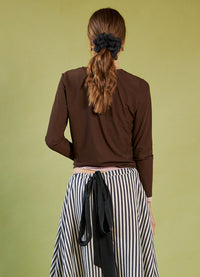 Woman wearing a Daylight Moon brown top and striped pants against a green background