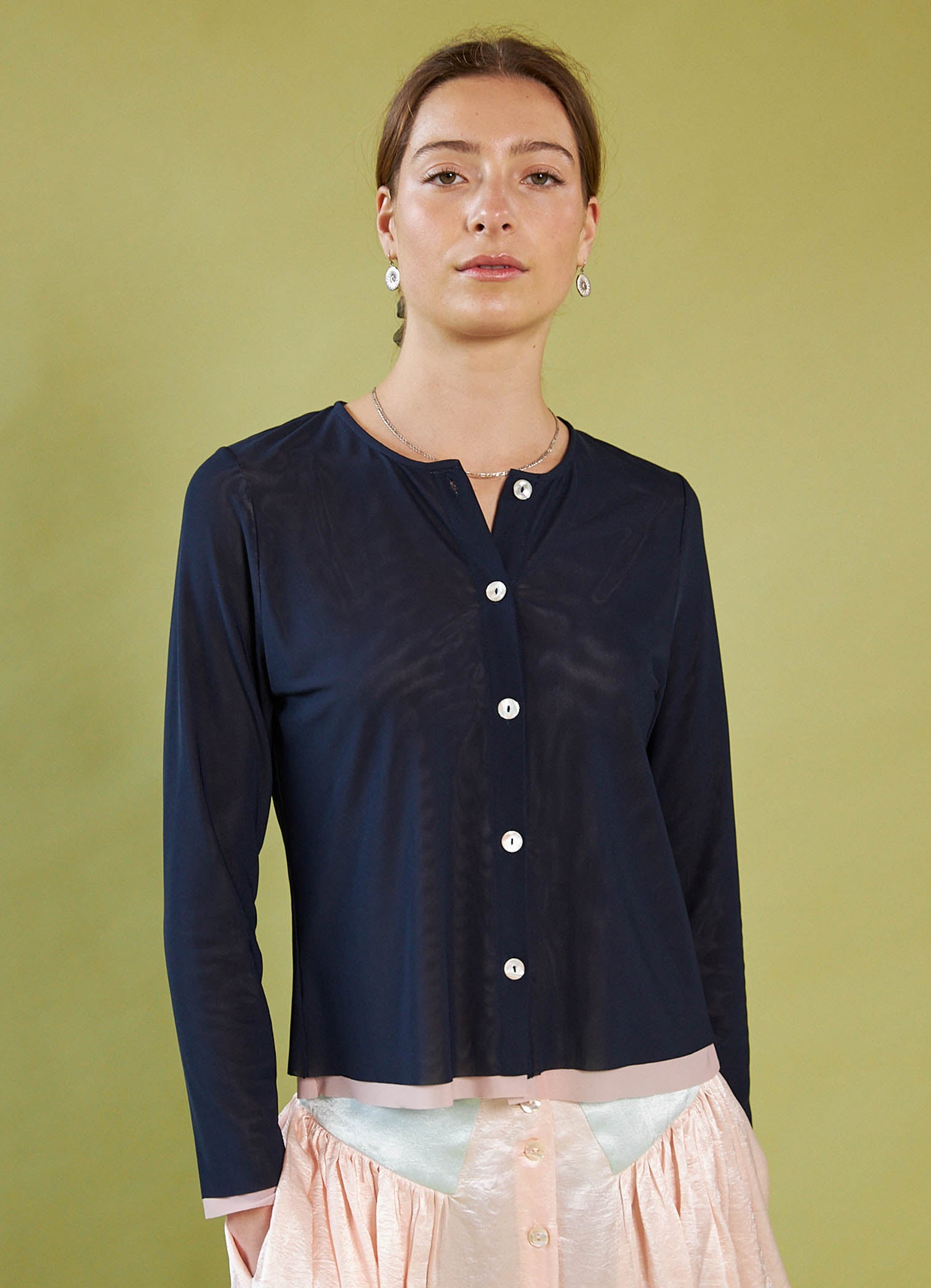 Woman wearing a Daylight Moon navy blue cardigan over a light pink dress against a green background