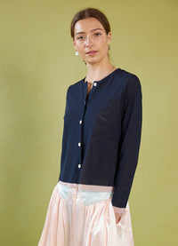 Woman wearing a Daylight Moon navy cardigan over a light blouse with pink skirts against a green background