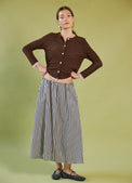 Woman wearing a Daylight Moon brown cropped cardigan and striped skirt on a green background